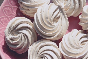 Beautiful light sweet dessert, meringues are a tea time treat or base for pavlova cake to calm a sugar rush. Crunchy cookies on pink ceramic plate.