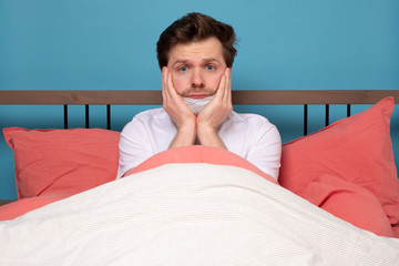 Sick mature caucasian man lying down in bed wearing mask protection mask