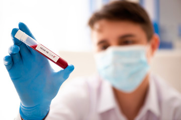 Test tube in male hand, doctor in medical mask holding vial with red liquid. Concept blood sample, Covid-19 coronavirus diagnostic, medical research