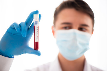 Test tube in male hand close up, doctor in medical mask holding vial with red liquid. Concept blood...