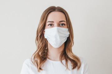 Portrait of a young girl in a medical mask isolated on a white wall background. Young woman...