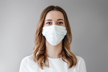 Portrait of a young girl in a medical mask isolated on white background. Young woman patient stands over grey background, copy space - Powered by Adobe