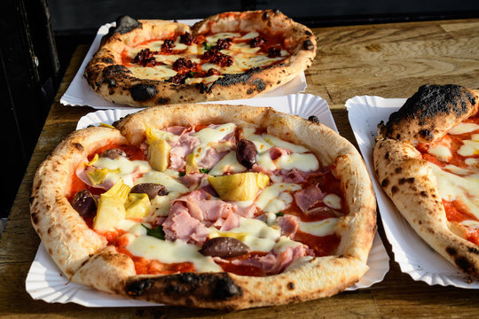 Traditional Italian pizza with prosciutto, artichoke and olives displayed for sale at a street food market festival in Bucharest, Romania, top view photo of healthy food photographed with soft focus