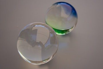 two individual glass balls against a gray background. One ball is crystal clear and the other shimmers green blue
