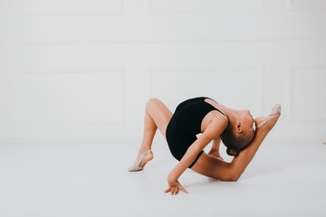 Young girl in a black dress doing gymnastics pose, forehead touches the heel, on white background