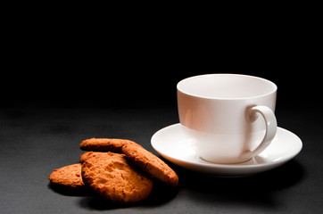 A white cup of coffee with homemade orange biscuits stands on black