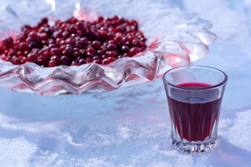 Alcoholic red tincture and red cranberries in an ice dish. Liquor in a glass stands in the snow. Focus on the glass. Horizontal.