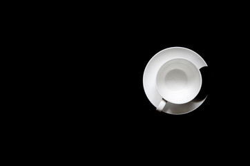 A white cup of coffee with black biscuits on a plate stands on a black background