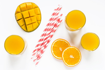 mango orange smoothies in glasses and paper tubes flat lay top view white background