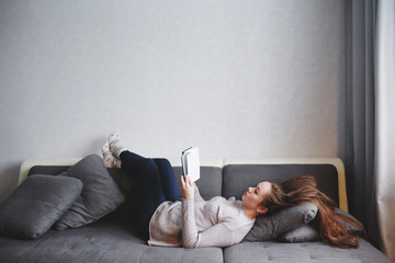Smart young female relaxing at home, reading book on the couch