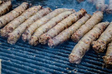 Mixed meat sausages being cooked on a hot black metallic grill in display for sale at a restaurant at a street food market, traditional food photographed with soft focus