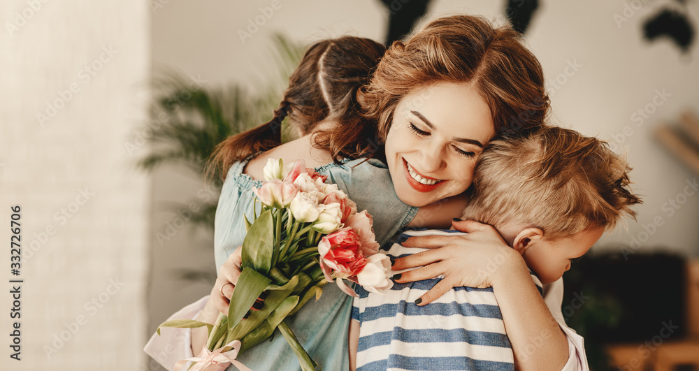 Wall mural little children congratulating and hug mother in kitchen.