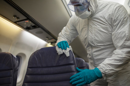 Worker in clean suit disinfecting airplane seats in COVID-19 pandemic