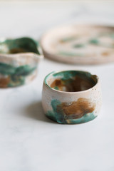 dishes made of white clay covered with green white and brown glaze after firing on a marble light background close-up. pottery top view of a glass, pitcher and plate