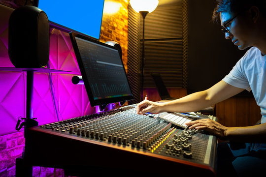 asian male sound engineer mixing music on audio mixing console in recording studio