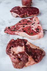 Different types of raw meat for steaks, T-bone, ribeye, fillet, sirloin on a marble desk.