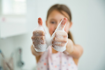 Little girl washing hands with water and soap in bathroom. Kid showing thumbs up. Hands hygiene and virus infections prevention.  - obrazy, fototapety, plakaty