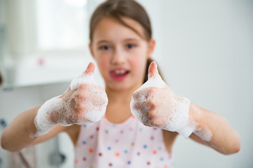 Little girl washing hands with water and soap in bathroom. Kid showing thumbs up. Hands hygiene and...