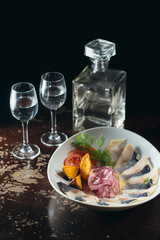 Traditional snacks salted herring with vegetables, onion, potato, tomato, two shots of vodka and a jug.