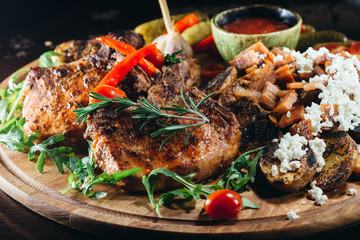 Appetizing plate with beef steaks with potatoes, hot chili peppers, beans and young potatoes, onions, cheese, pickled cucumners and a red sauce.