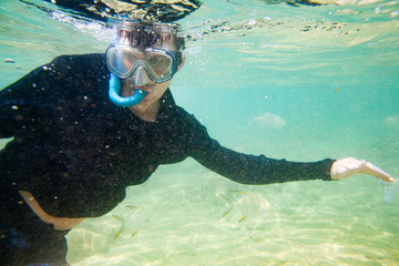 A man swims with a camera in a mask under water with colorful fish.