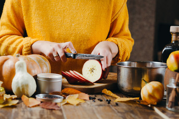 Close-up photo of woman's hands in yellow sweater cutting apples for hot wine. Winter cozy holidays mood.