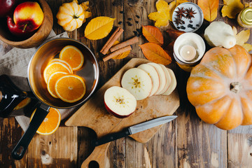 Flatlay with ingredients for cooking mulled wine. Cutted apples on a wooden board, oranges, cinnamon sticks, anise stars, cardamon, pimpkins and candles.