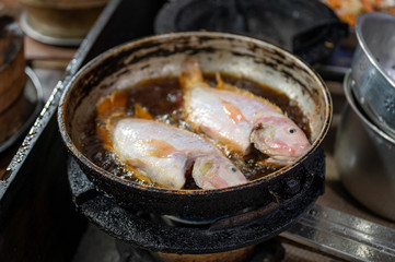 Two red tilapia fish frying with bubbling in dirty pan