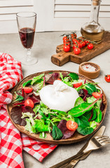 Salad with Italian burrata cheese, arugula, spinach, cherry tomatoes and olive oil served on wooden plate with wine. Selective focus. Light gray concrete background