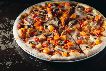 Italian pizza with melted cheese, tomatoes, chili pepper, mushrooms and herbs on a brown table. Tasty hot pizza.