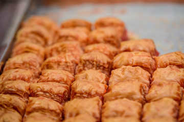 Close up of traditional oriental sweet pastry cookies known as backlava, Turkish desert with sugar, honey, walnuts and pistachio, in display at an weekend street food market, top view, soft focus