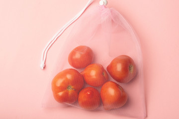 A ripe branch of tomato in a reusable reuse bag on a pink blue background. Eco friendly alternative to plastic bags.