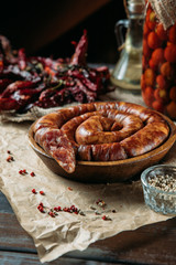 Side view of tasty traditional long sausage in a wooden bowl, dried peppers, spices and oil on the table.