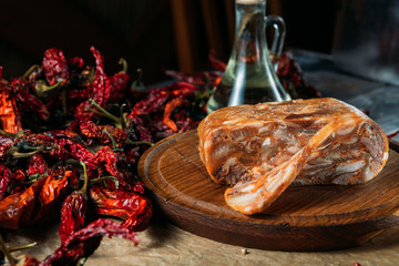 Large piece of traditional dish head cheese and its slice on wooden cutting board on craft paper,...
