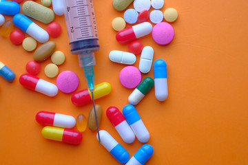  colorful pills and syringe on orange background, top view