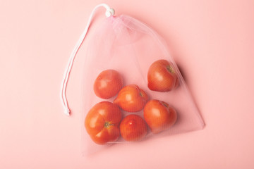 A ripe branch of tomato in a reusable reuse bag on a pink blue background. Eco friendly alternative to plastic bags.