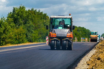 Road repair, compactor lays asphalt. Heavy special machines. Asphalt paver in operation. Side view....
