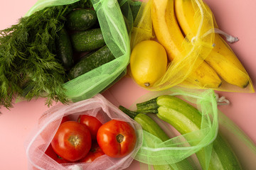 Vegetables and fruits in grocery mech on pink background. Bananas, parsley, zuzzini, cucumbers top view.