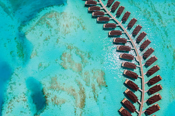 The drone photo with a wooden water villas seen from above and an amazing blue lagoon crystal clear water close to tropical lagoon. Amazing summer travel and vacation background. Dreamy beach scenery
