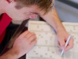 Closeup of a man holding a pencil solving crosswords wearing a red shirt in his free time.