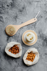 Spa and wellness flat lay on concrete grey background. Body care and cellulite treatment tools, mesh bags with almonds and chestnuts. Natural brush for dry skin peeling or massage and luffa sponge