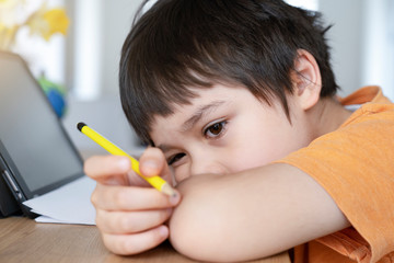School kid in self isolation using tablet for homework,Bored Child sad face lying head down looking out deep in thought, Boy stay at home during covid-19 lock down, Distance learning online education