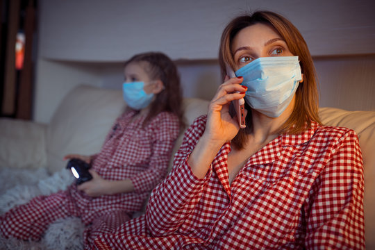 Woman With Little Kid At Home Isolation Auto Quarantine Wearing Face Mask With Smart Phone For Reading Information About Coronavirus Disease 2019.