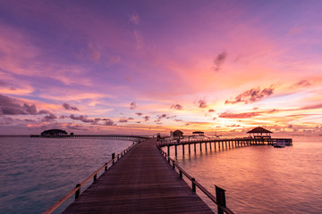 Fototapeta premium Sunset on Maldives island, luxury water bungalows villas resort and wooden pier. Beautiful sky and clouds and beach with seascape for summer vacation holiday and travel concept