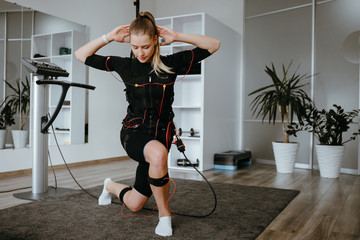 EMS training. Front view of young woman doing front lunges in suit with cables. - obrazy, fototapety, plakaty