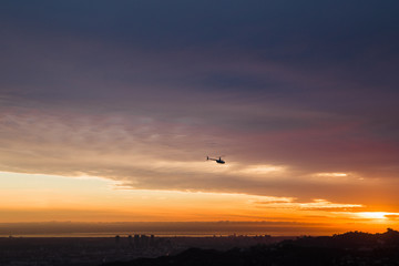 helicopter flies above city at sunset
