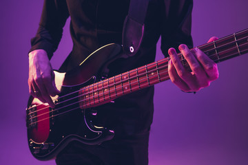 Obraz na płótnie Canvas Young and joyful caucasian musician playing guitar on gradient purple studio background in neon light. Concept of music, hobby, festival. Colorful portrait of modern artist. Attented and inspired.