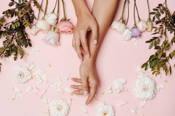 Woman's hands and white, pink and purple flowers and green branches, petals on the pink background.