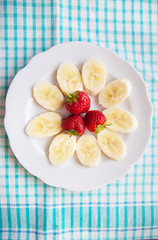banana and strawberries on a white plate and a colorful napkin