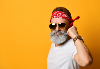 Grandpa in sunglasses, red bandana, white t-shirt and bracelet. He straightens his mustache, posing...